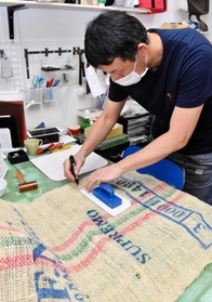 コーヒー豆の入っていた麻袋から使用する部分を切り出す中野嘉容さん＝カバンツクリエーション０２０３