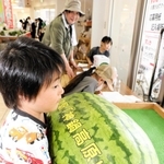 ジャンボスイカに両手を回し、重さを予想する子ども＝道の駅「神鍋高原」