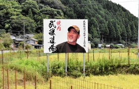 田んぼの中に突如現れる武藤敬司さんの看板＝豊岡市岩熊