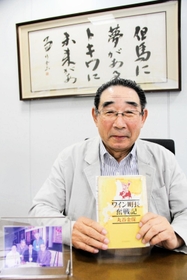 梨ワイン造りのきっかけとなった書籍「ワイン町長奮戦記」を手にする柴崎一秀会長＝香美町香住区三谷