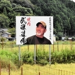 田んぼの中に突如現れる武藤敬司さんの看板＝豊岡市岩熊