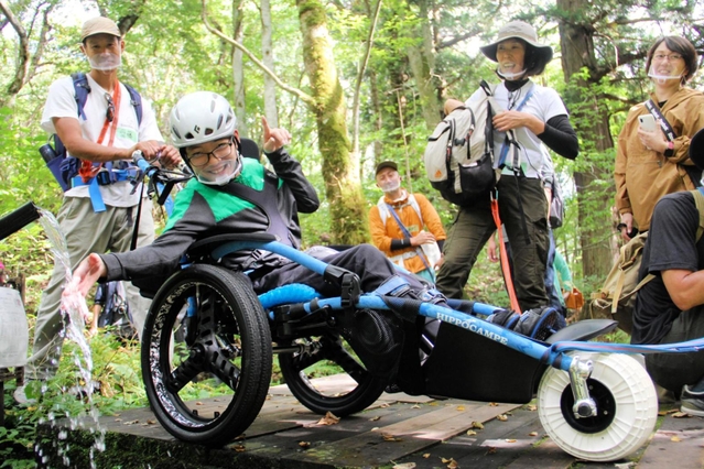 水陸両用車いすから湧き水に触れて笑顔を見せる小林快多さん＝たじま高原植物園