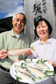なれずしを販売する田中勝英さん（左）と真智子さん夫妻。勝英さんの手には大物の「尺アユ」＝道の駅「あゆの里矢田川」