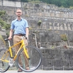 自転車を支えながら、神子畑選鉱場跡の前に立つケビンさん＝朝来市佐嚢