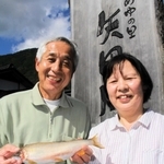 なれずしを販売する田中勝英さん（左）と真智子さん夫妻。勝英さんの手には大物の「尺アユ」＝道の駅「あゆの里矢田川」