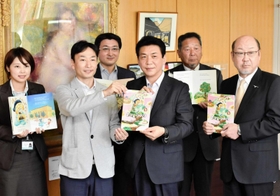 関貫久仁郎市長（前列右から２人目）に絵本を手渡す今井秀司さん（同３人目）＝豊岡市役所
