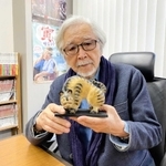 木彫フォークアートへの思いを語る山田洋次監督。養父市大屋町在住の作家、松田一戯さんが贈ったえとの置物を手にする（養父市提供）