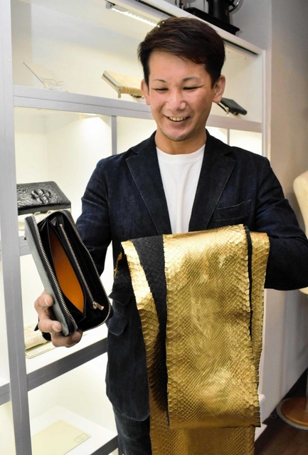 金箔を施したヘビ革を内側に使用した財布を手にするオーナーの土生田直樹さん＝豊岡市中央町
