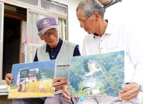 撮影したコウノトリの写真を持つ兄の水嶋芳彦さん（左）と安夫さん＝豊岡市日高町