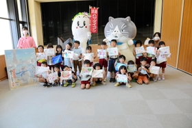浜坂認定こども園の園児２１人と集合写真をとるマル（右）とハマダイコン＝加藤文太郎記念図書館