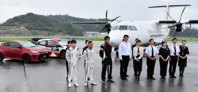 滑走路で飛行機とスポーツカーの前で記念撮影をする関係者ら＝但馬空港