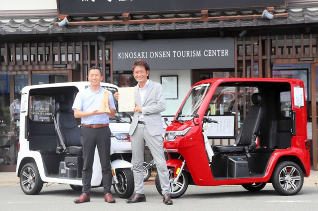 電動三輪車トゥクトゥクの前で、受賞の記念撮影に納まるたびぞうの大林大悟代表取締役（右）＝豊岡市城崎町湯島