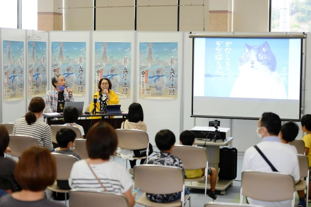 かなしきデブ猫ちゃんの物語を読み聞かせする俳優の河合美智子さん、峯村純一さん夫妻＝但馬空港