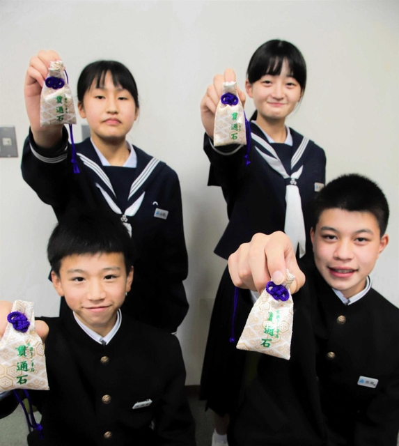 笠波トンネルの貫通石が入ったお守りを掲げる生徒たち＝村岡中学校
