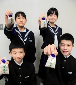 笠波トンネルの貫通石が入ったお守りを掲げる生徒たち＝村岡中学校