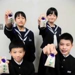 笠波トンネルの貫通石が入ったお守りを掲げる生徒たち＝村岡中学校