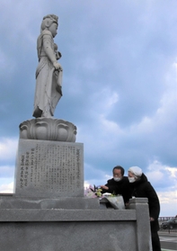 慰霊碑の観音菩薩（ぼさつ）像に花を手向ける藤崎光子さん＝香美町香住区余部