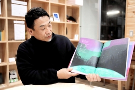 お気に入りの絵本「世界はこんなに美しい」を紹介する伊藤善則さん。パリで暮らす女性がバイクにまたがり、世界一周を目指す物語だ＝ＪＲ香住駅