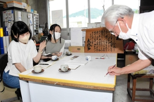 松下重則さんからレタリングの技術を教わる永井楓華さん（左）と長谷言意さん＝朝来市和田山町東谷