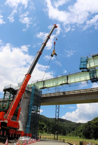 クレーンで鉄製の橋桁をつり下げ、橋を延ばしていく作業が続く工事現場＝豊岡市上佐野
