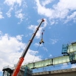 クレーンで鉄製の橋桁をつり下げ、橋を延ばしていく作業が続く工事現場＝豊岡市上佐野