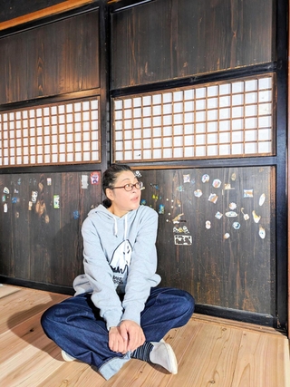 引っ越し先でお気に入りの建具の前に座る河合美智子さん＝豊岡市内（本人提供）