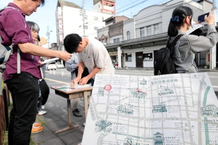 「豊岡復興建築群」に施された装飾のデザインスタンプを、オリジナルマップに押す参加者たち＝豊岡市中央町