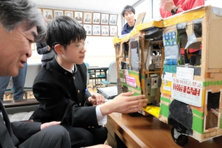 段ボールで作った全但バスの模型を、村上宣人社長（左）に説明する足立陸弥さん＝豊岡聴覚特別支援学校