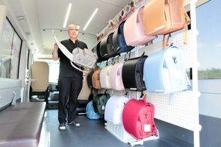 ランドセルが並ぶマイクロバスの車内で、主力商品を手にする宿南孝弘社長＝豊岡市九日市下町