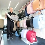 ランドセルが並ぶマイクロバスの車内で、主力商品を手にする宿南孝弘社長＝豊岡市九日市下町