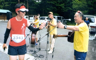 「みかた残酷マラソン全国大会」のランナーとハイタッチする高石ともやさん＝２０１６年６月１２日、香美町小代区忠宮（久保井洋次さん提供）