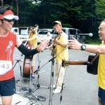 「みかた残酷マラソン全国大会」のランナーとハイタッチする高石ともやさん＝２０１６年６月１２日、香美町小代区忠宮（久保井洋次さん提供）