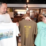 豊岡市日高町の地名や八代オクラがデザインされたＴシャツ。「農家さんがよく着ているオリーブ色は外せなかった」と話す冨樫実和さん（右）＝豊岡市日高町