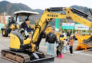 社員と一緒に運転席に座り、ミニショベルカーの操作を体験する児童ら＝養父市薮崎