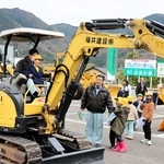 社員と一緒に運転席に座り、ミニショベルカーの操作を体験する児童ら＝養父市薮崎