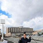昨年１１月に入院した公立豊岡病院を背景に立つ河合美智子さん＝豊岡市戸牧（本人提供）