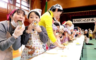 ２０メートルを超える長い巻きずしを切って食べる参加者たち＝中竹野ふるさと館