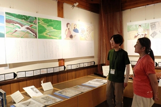 コウノトリの保護増殖に尽力した松島興治郎さんの歩みを紹介する紙芝居。物語を手がけた山下美登理さん（右）、イラストを担当した桐島杏莉さん＝豊岡市祥雲寺