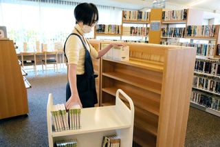 増設した書架に時代小説の文庫本を並べる図書館員ら＝養父市八鹿町八鹿