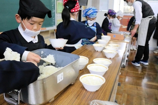 学校給食で提供されている無農薬のコウノトリ育むお米を配膳する子どもたち＝豊岡市庄境
