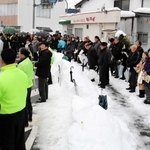 雪が積もった豊岡市内で立候補者の主張を聞く支持者ら＝同市泉町