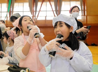 恵方の「南南東」を向き、完成した巻きずしを頰張る子どもたち＝豊岡市竹野町轟