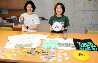 城崎と神鍋地域で販売するグッズを手にする（左から）豊岡観光イノベーションの谷垣千恵さんと佐野祥子さん＝豊岡市大磯町