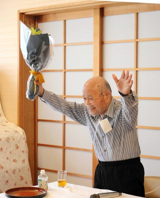 講演を終えて花束を受け取り、拍手に両手を挙げて応えた山下幸雄さん＝２０２５年８月、豊岡市但東町中山