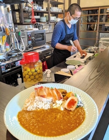 キッチンで料理する居相さん。手前は、丹波鶏や地元の野菜を生かしたスパイスカレー＝丹波篠山市立町