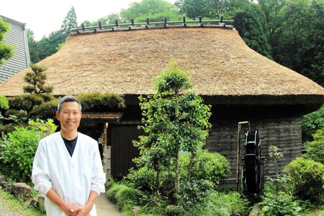 茅葺き屋根の葺き替えを終えた建物の前に立つ「いわや」の店主・岩本和也さん＝丹波篠山市火打岩