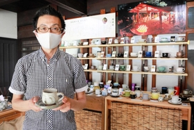 「珈琲豆　誠」の店主佐藤誠一さん。専用の棚には丹波焼の約６０窯元のコーヒーカップが並ぶ＝丹波篠山市西町