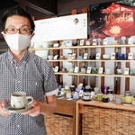 「珈琲豆　誠」の店主佐藤誠一さん。専用の棚には丹波焼の約６０窯元のコーヒーカップが並ぶ＝丹波篠山市西町