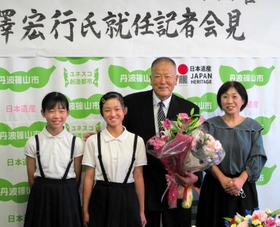 丹波篠山市スポーツ振興官の就任が決まり、会見した長沢宏行さん（右から２人目）。小学生から花束を受けて記念撮影した＝丹波篠山市役所