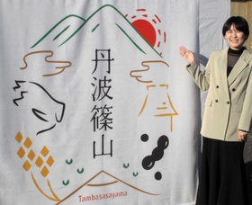 作者の岡田さんとブランドロゴ。「市名の周りに宝石があふれているイメージにした」という＝丹波篠山市北新町